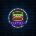 Neon glowing sign of burger in circle frame on a dark brick wall background. Fastfood light billboard symbol.