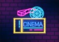 Neon glowing signboard for cinema with film disk and tape on brick wall. Movie theatre illuminating electric decorative