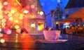 Neon night city blurred light street restaurant yellow coffee cup lantern on wooden table medieval house in Tallinn Old Town Eston