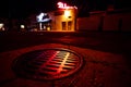 Neon night city life lighting with red and orange sewer cap on asphalt