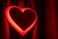 Neon red heart sign glowing against a dark curtain, symbolizing love