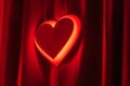 Neon red heart sign glowing against a dark curtain, symbolizing love Royalty Free Stock Photo