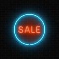 Neon red sale sign in a blue circle frame on a dark brick wall background. Round the clock big discount signboard.