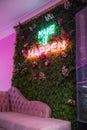 Neon sign on wall of green leaves above pink couch