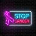 Neon stop cancer glowing sign on a dark brick wall background. Pink ribbon as a cancer awareness month. Royalty Free Stock Photo