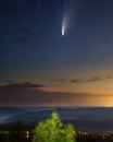 Neowise comet in the starry sky over the forest with city lights on the background