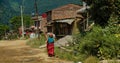 Older woman carries a heavy bag on her back through the poverty stricken village