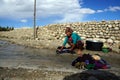 Nepal. Tsarang. Nepalese woman is washing clothes in a creek in the street, against the backdrop of a stone wall.