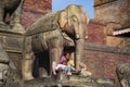 Nepali mother and baby sit under elephant statue of Hindusim temple , Kathmandu , Nepal