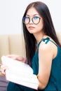 Nerd asian girl sitting on bed while reading book in a living room Royalty Free Stock Photo