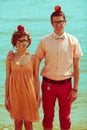 Nerds` honeymoon concept. Portrait of couple of young happy married hipsters in trendy clothes standing together on the beach wit Royalty Free Stock Photo
