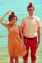 Nerds` honeymoon concept. Portrait of couple of young happy married hipsters in trendy clothes standing together on the beach wit Royalty Free Stock Photo