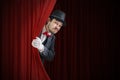 Nervous actor or illusionist is hiding behind red curtain in theater