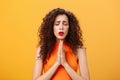 Nervous and concerned woman with curly hairstyle feeling hopeful praying with closed eyes and frowned eyebrows holding