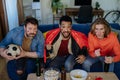 Nervous football fans friends staring at TV and watching football match at home