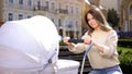 Nervous young woman trying to calm down crying baby in stroller, baby colic