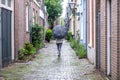 Netherlands, Leiden town. Lady with umbrella walks between traditional red brickwall buildings