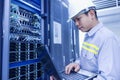 Network administrator holding laptop in hand working Configuration with core switch on rack cabinet in data center