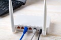 Network cables connected to a white Wi-Fi wireless router near laptop on a white wooden table. Wlan router with internet cables Royalty Free Stock Photo