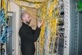 A network engineer connects two patch cord in the server room of the data center. A specialist works among the disorderly