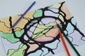 Neurographic drawing of abstract shapes and black lines, colored with colored pencils. Several colored pencils lie near the