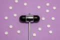 Neurological metallic reflex hammer lies on purple background surrounded by white pills. The idea of photo of diagnostics and trea