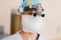 Neurosurgeon man in a white mask in special medical clothes in magnifying glasses with binocular loupes is in a hospital.