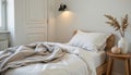 neutral bedroom with folded throw blanket, soft linen sheets, blank pottery on the side table, and warm wall light Royalty Free Stock Photo