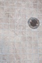 A neutral light beige square tile shower floor with a silver metal drain