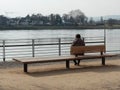 Neuwied, Germany - March 23, 2021: a woman seen from behind, sitting on a bench - symbol for loneliness in Corona pandemic