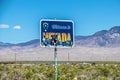 Welcome to Nevada sign with stickers partly covering it with wire fence and desolate purple mountains Royalty Free Stock Photo