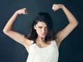 Never apologize for being a powerful woman. Studio shot of a beautiful young woman flexing her muscles against a dark