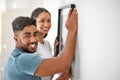 Never forget about picture frames. a young couple putting a picture frame up on their wall in their new home. Royalty Free Stock Photo