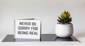 Never regret being real. Inspirational phrase on notepad, next to a cactus flower on a white and black background.