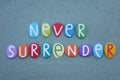 Never surrender, motivational message composed with multi colored stone letters over green sand