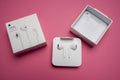 New Apple Earpods, Airpods white earphones for listening to music and podcasts in an open box. Isolated pink background. Budapest