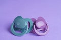 New baby pacifiers on purple background, closeup