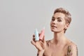 New Beauty. Portrait of beautiful tattooed woman with pierced nose and short hair holding plastic bottles with cosmetic