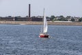 Red sailboat crossing New Bedford outer harbor