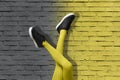 New Black female sneakers on long slender girl legs in yellow tights on background of gradient yellow and gray brick wall. Color Royalty Free Stock Photo