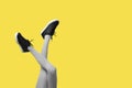 New Black female sneakers on long slender woman legs in gray tights isolated on yellow background Royalty Free Stock Photo