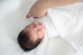 New born baby smiling while mother`s hand swaddling her body with white blanket.