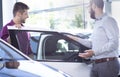 New buyer getting into a car in a showroom. Car dealer standing