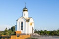 A new chapel next to the road and village in the countryside with white walls and a golden dome with a cross against the backdrop