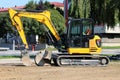 New compact excavator left on side of the main road at local construction site surrounded with gravel and tall trees