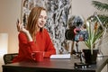 New content! Young female blogger speaking in front of camera and holding a pen in hand while sitting indoors