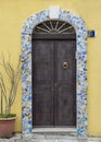 New dark brown wooden door with a stone arch decorated with broken patterned tiles in Italy