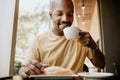 New day welcome.Young attractive African man enjoying his morning coffee and french croissant while sitting at modern