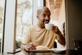 New day welcome.Young confident African man enjoying his morning coffee and french croissant while sitting at modern