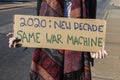 New Decade-Same War Machine - woman in scarf holds homemade sign